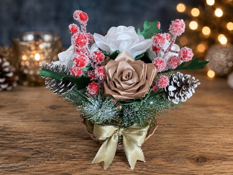 Handmade gold, white and cream Christmas floral arrangement with ribbon roses, frosted berries and festive greenery.